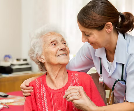 Elderly woman looking lovingly up at carer who has arms around her